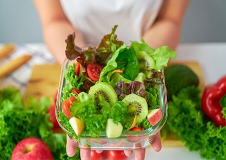 Pessoa segurando recipiente de vidro com salada de folhas e frutas