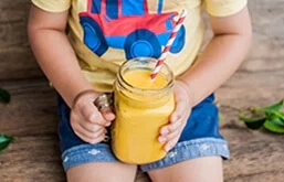 Criança sentada segurando copo de suco