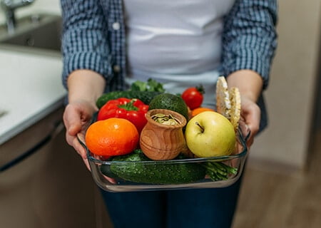 Pessoa segurando pote de vidro com diversos alimentos como frutas e vegetais