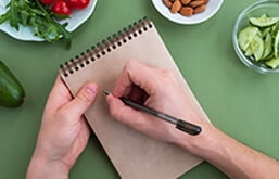 Mão anotando em caderneta sobre mesa com bowls de alimentos