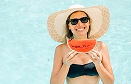 Mulher segurando fatia de melancia na piscina, um dos alimentos que ajudam a manter o bronzeado
