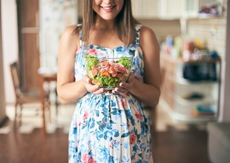 Mulher grávida segurando pote de salada