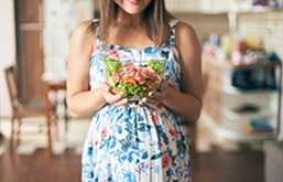 Mulher grávida segurando pote de salada