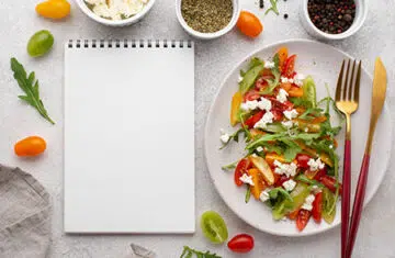 Mesa com prato de salada e caderno