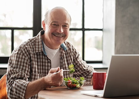 Homem idoso comendo salada e sorrindo