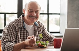 Homem idoso comendo salada e sorrindo
