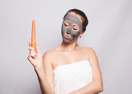 Mulher com máscara no rosto e segurando cenoura