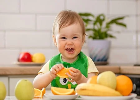 Bebê com fatia de laranja na mão sorrindo