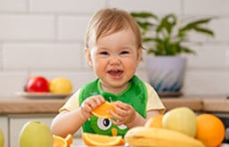 Bebê com fatia de laranja na mão sorrindo