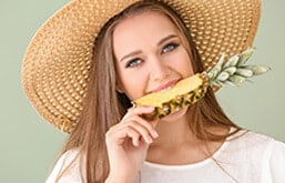Mulher comendo abacaxi, um dos alimentos que causam aftas