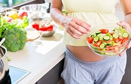 Mulher grávida na cozinha segurando pote com saladas