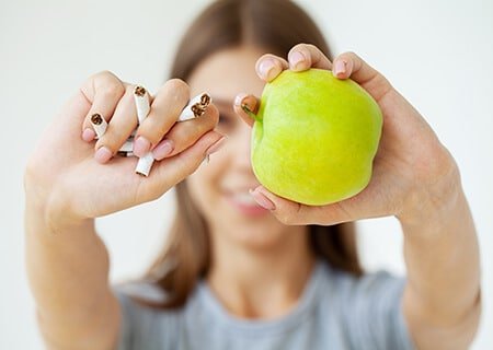 Mulher segurando cigarros em uma mão e uma maçã verde em outra