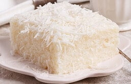Fatia de bolo de tapioca granulada em prato com xícara de café e guardanapo de pano ao fundo