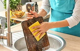 Pessoa lavando tábua de madeira com esponja na pia