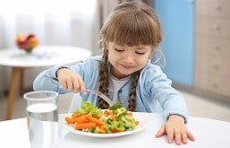 Menina comendo prato de legumes