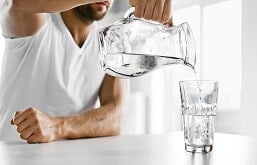 Homem colocando água em um copo de vidro