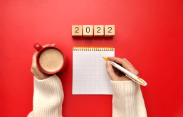 Escrevendo metas para 2022 em uma bloco de anotações com um café em uma mão e uma caneta em outra