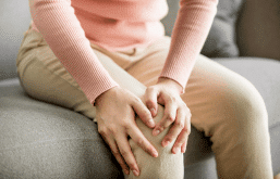 Mulher colocando as mãos no joelho por conta da dor