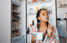 Mulher tomando sorvete em frente à geladeira