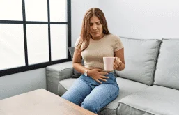 Mulher tomando chá e com a mão na barriga