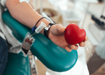 Mão segurando coração de borracha para doar sangue