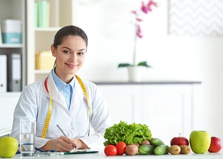 Nutricionista sorrindo atrás de mesa com verduras
