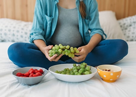 Mulher grávida sentada na cama com tigelas de frutas