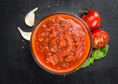 Molho de tomate em tigela com pedaços de tomate e alho ao lado