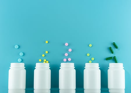 Caixas brancas de medicamentos com pílulas de suplementos coloridas saindo de dentro deles