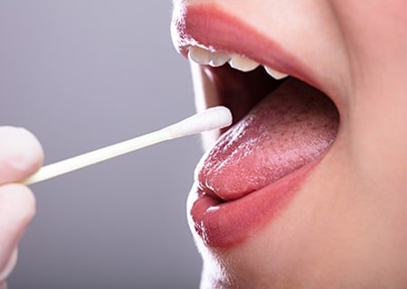 Pessoa com a boca aberta com bastão para teste de saliva dentro
