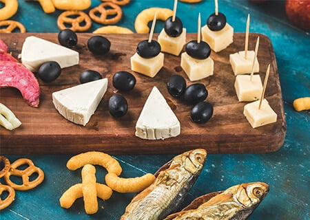 Mesa com alimentos ricos em sódio, como azeitonas, queijos, salgadinhos e peixes em conserva. Crédito da imagem: azerbaijan_stockers/Freepik.
