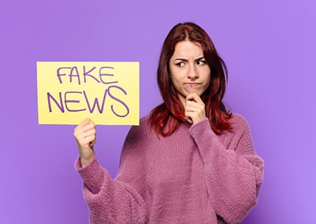 Mulher segurando placa escrito "fake news"