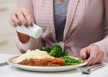 Mulher colocando sal em prato de comida